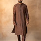 Man wearing a brown embroidered kurta with pants against a textured beige wall.