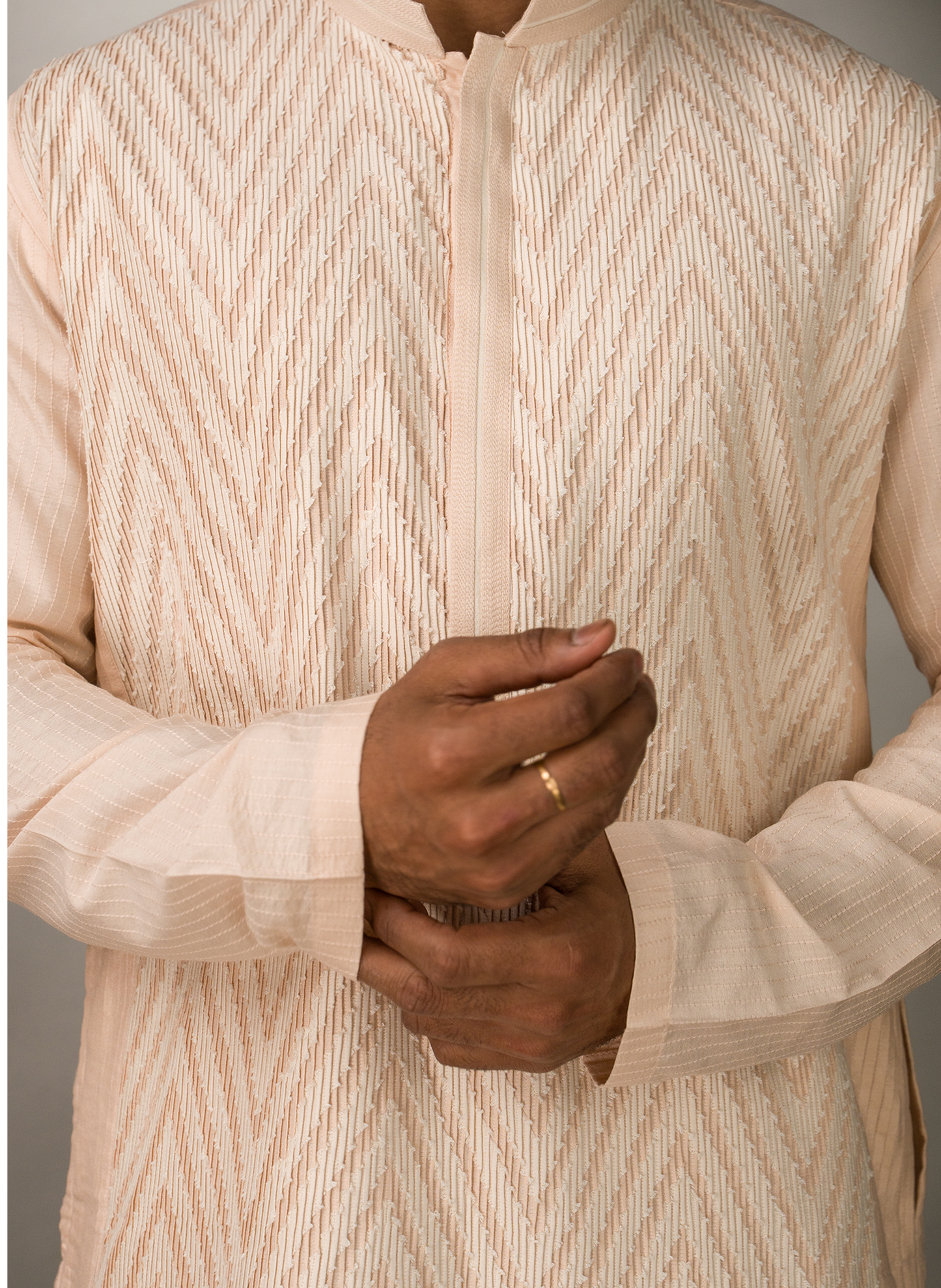 Close-up of a person wearing a pink patterned kurta with hands clasped together.